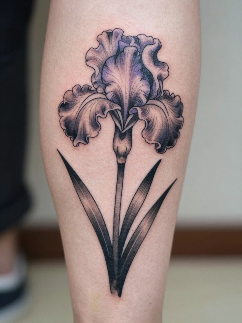 close-up of a Japanese iris tattoo on the calf, tall elegant petals and leaves, black and grey ink with soft violet accents, clean traditional linework, soft shading, realistic skin texture, design-focused close-up, blurred neutral background, modern tattoo photography (no watermarks on images)