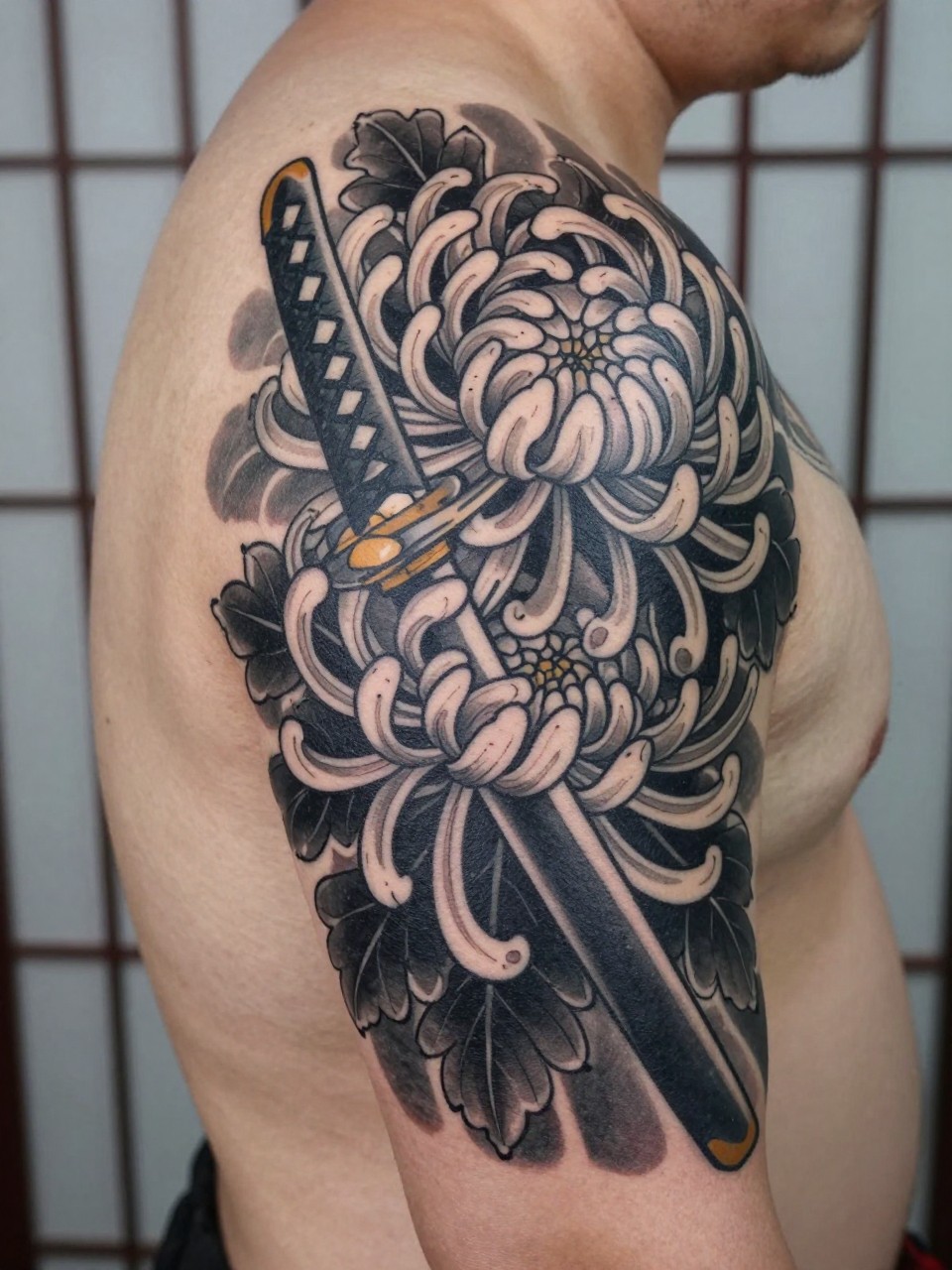 design-focused close-up of a full back Japanese sword and chrysanthemum tattoo on a man, katana details crossing large chrysanthemum blooms, black and grey ink, bold traditional linework, soft shading, realistic skin texture, minimal blurred background (no watermarks on images)
