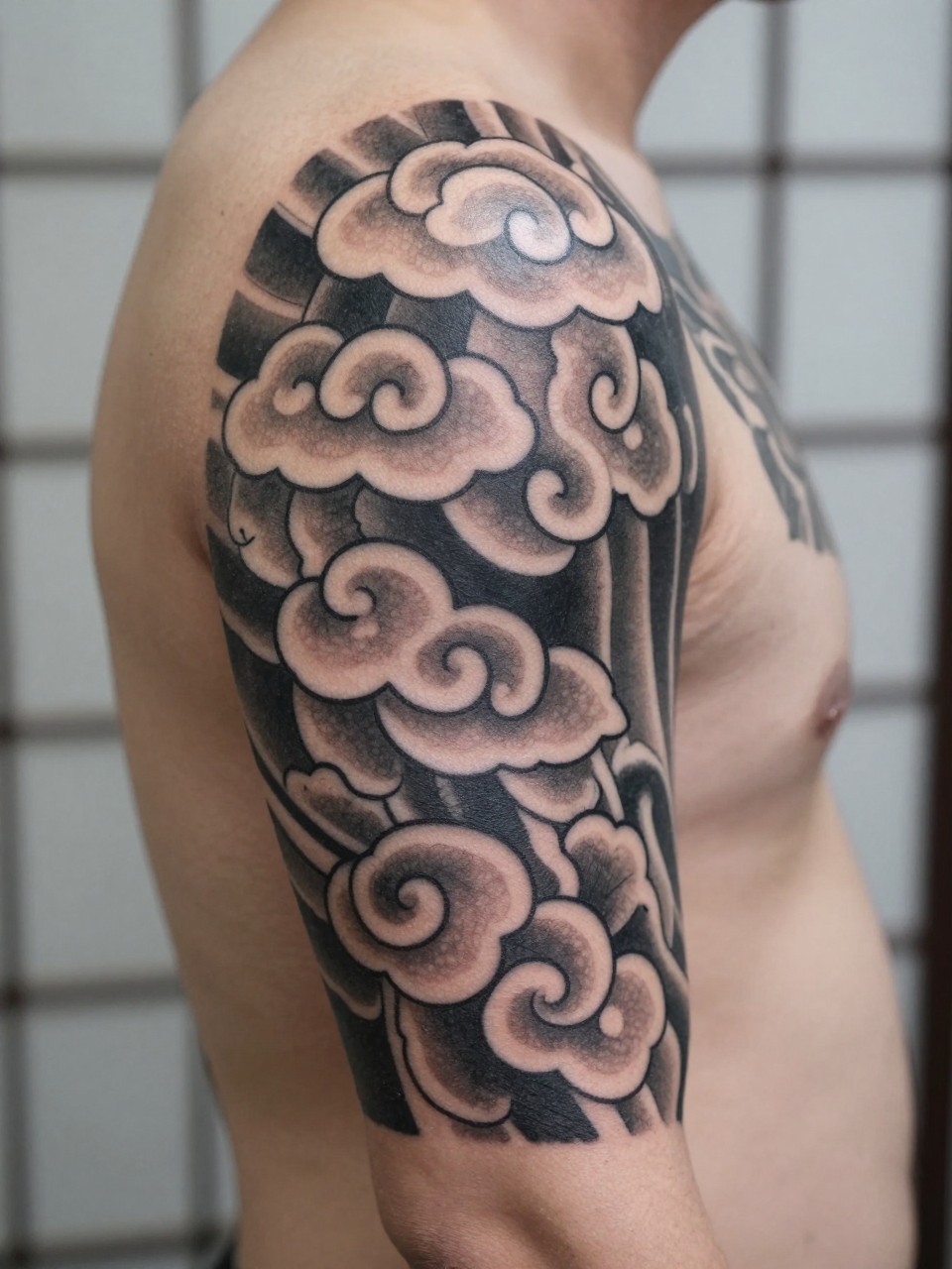 close-up of a Japanese cloud armband tattoo on a man's upper arm, repeating traditional cloud forms wrapping around the arm, black and grey ink, crisp linework, soft shading, clean masculine composition, realistic skin texture, design-focused close-up, blurred neutral background, modern tattoo photography (no watermarks on images)