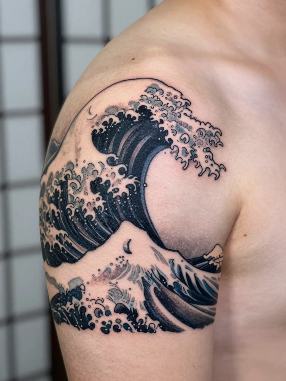 design-focused close-up of a clean Japanese wave and moon tattoo on the shoulder, bold wave curl, small crescent moon detail, black and grey ink, fine traditional linework, soft shading, realistic skin texture, minimal blurred background, modern tattoo inspiration photo (no watermarks on images)