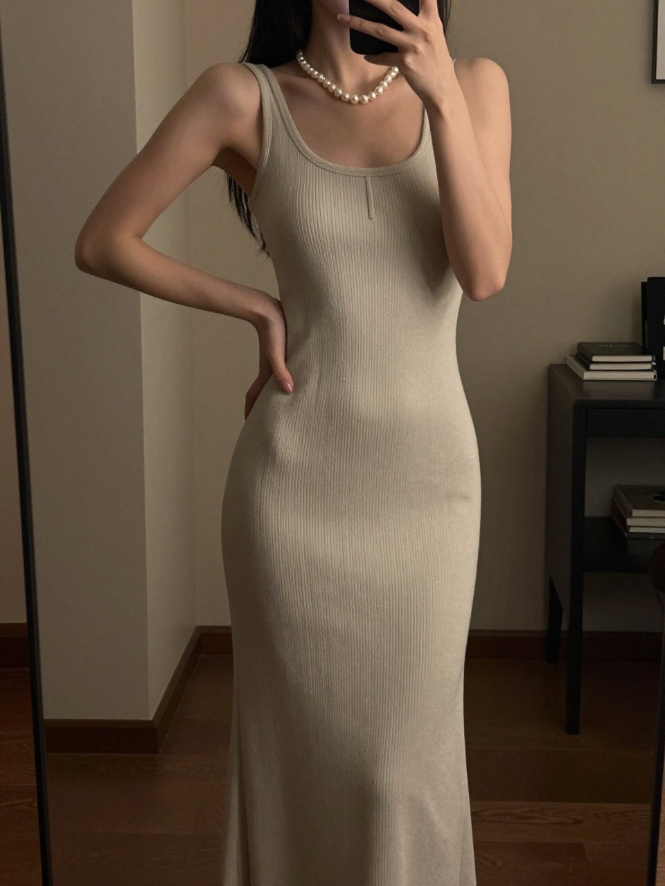 iPhone mirror selfie of a woman in a column maxi dress with pearl jewelry, hand on hip, cropped at NECK so face doesn't show, in a city apartment, warm moody lighting, iPhone photo quality.