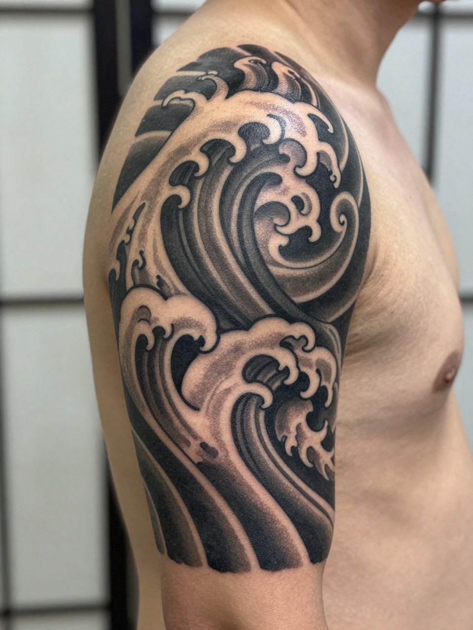 close-up of a blackwork Japanese wave armband tattoo on a man's upper arm, bold curling wave forms wrapping around the arm, heavy black ink, strong contrast, traditional-inspired linework, realistic skin texture, design-focused close-up, blurred neutral background, modern tattoo photography (no watermarks on images)