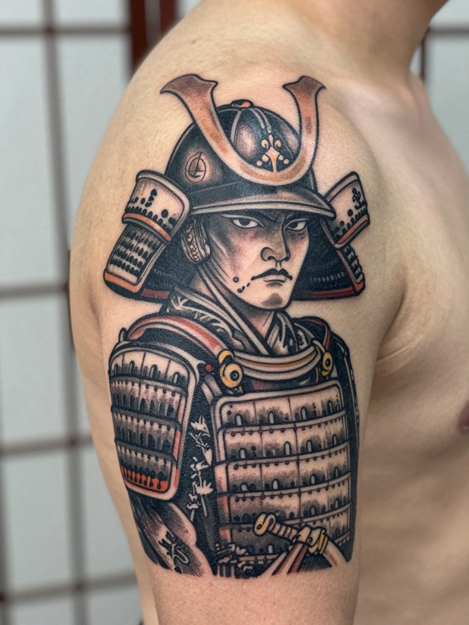 close-up of a traditional Japanese samurai warrior tattoo on the arm, detailed armor, helmet crest, sword accents, bold black and grey ink, strong linework, soft shading, realistic skin texture, design-focused close-up, neutral blurred background, modern tattoo photography (no watermarks on images)