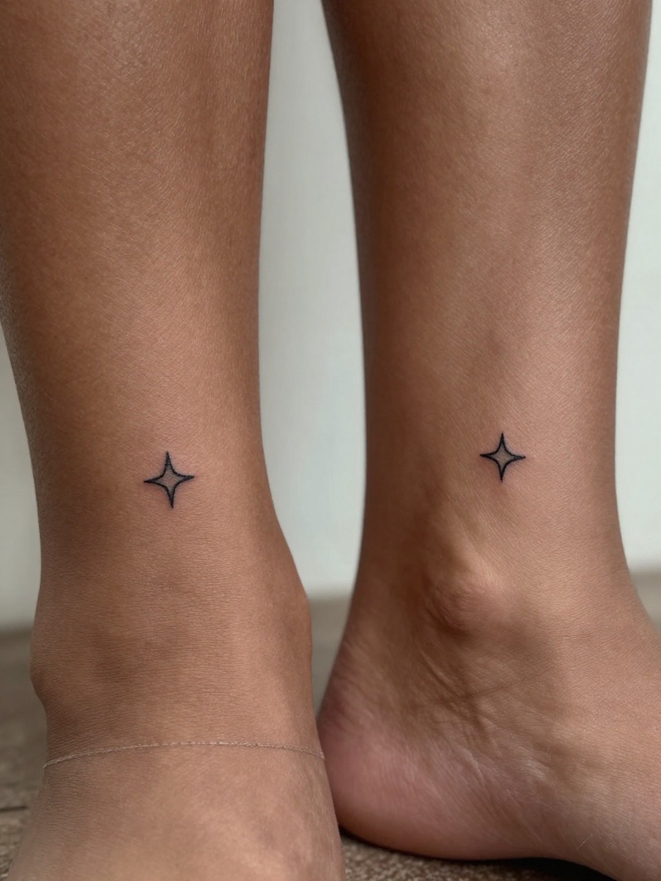 "close-up of matching tiny star tattoos on deep brown skin, one on each ankle, crisp black ink, fine line minimalist star shapes, realistic skin texture, delicate anklet visible, design-focused close-up, soft blurred background, modern tattoo photography (no watermarks on images)"