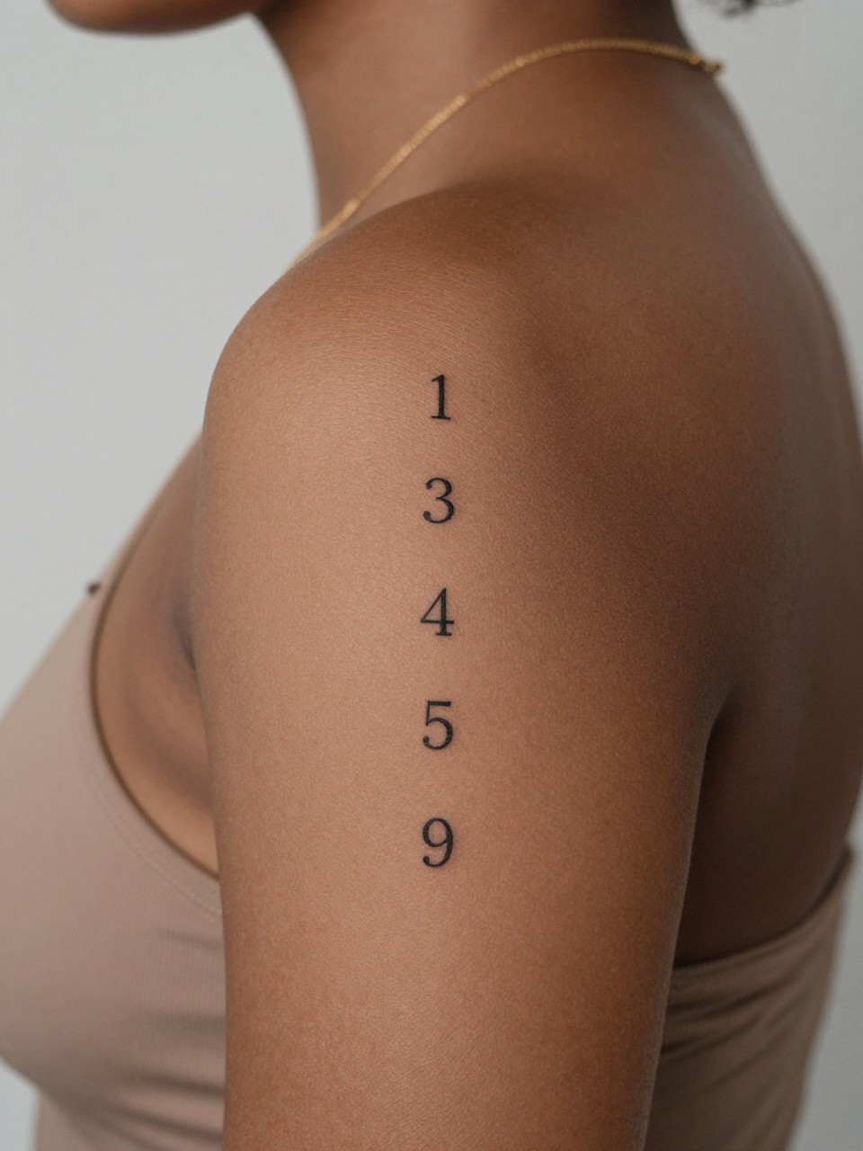 design-focused close-up of a vertical angel number spine tattoo on rich brown skin, clean black ink numbers aligned down the spine, fine line minimalist style, realistic skin texture, delicate gold necklace at the neck, minimal blurred background, modern feminine tattoo inspiration photo (no watermarks on images)