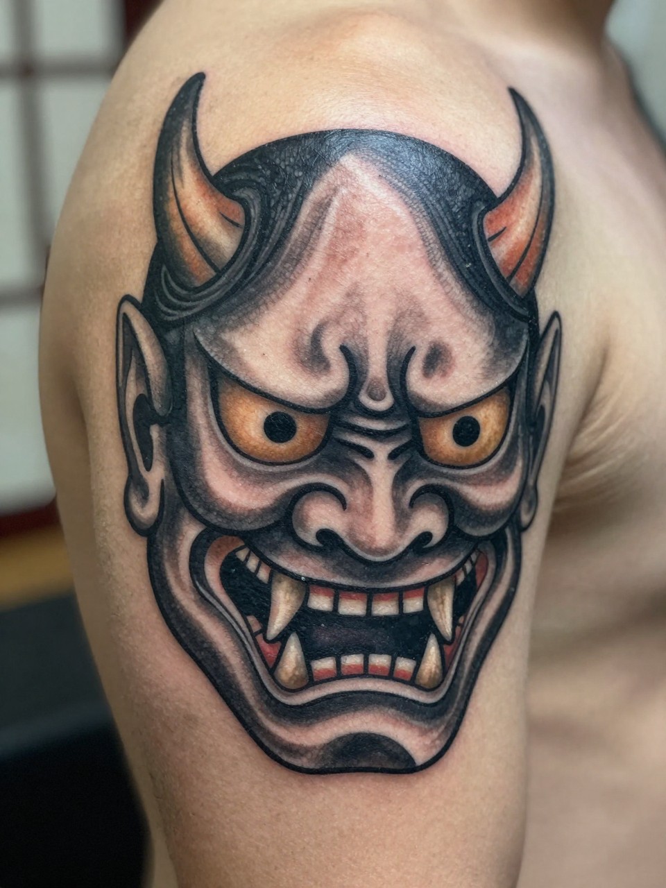 close-up of a traditional Japanese Oni mask tattoo on the back of the hand, bold demon face, curved horns, sharp teeth, black and grey ink, dramatic shading, thick traditional linework, realistic skin texture, design-focused close-up, neutral blurred background, modern tattoo photography (no watermarks on images)