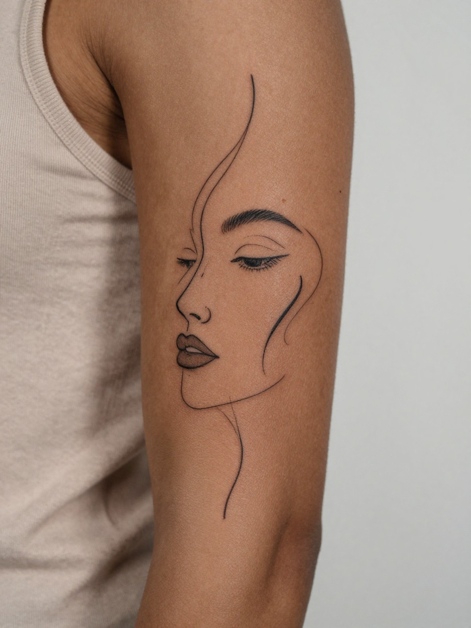 macro shot of an abstract line art sleeve tattoo on deep brown skin, flowing black ink curves, modern face outline elements, minimalist artistic composition across the arm, fine line work, realistic skin texture, neutral sleeveless top visible, design-first close-up, soft minimal background, feminine tattoo inspiration photography (no watermarks on images)