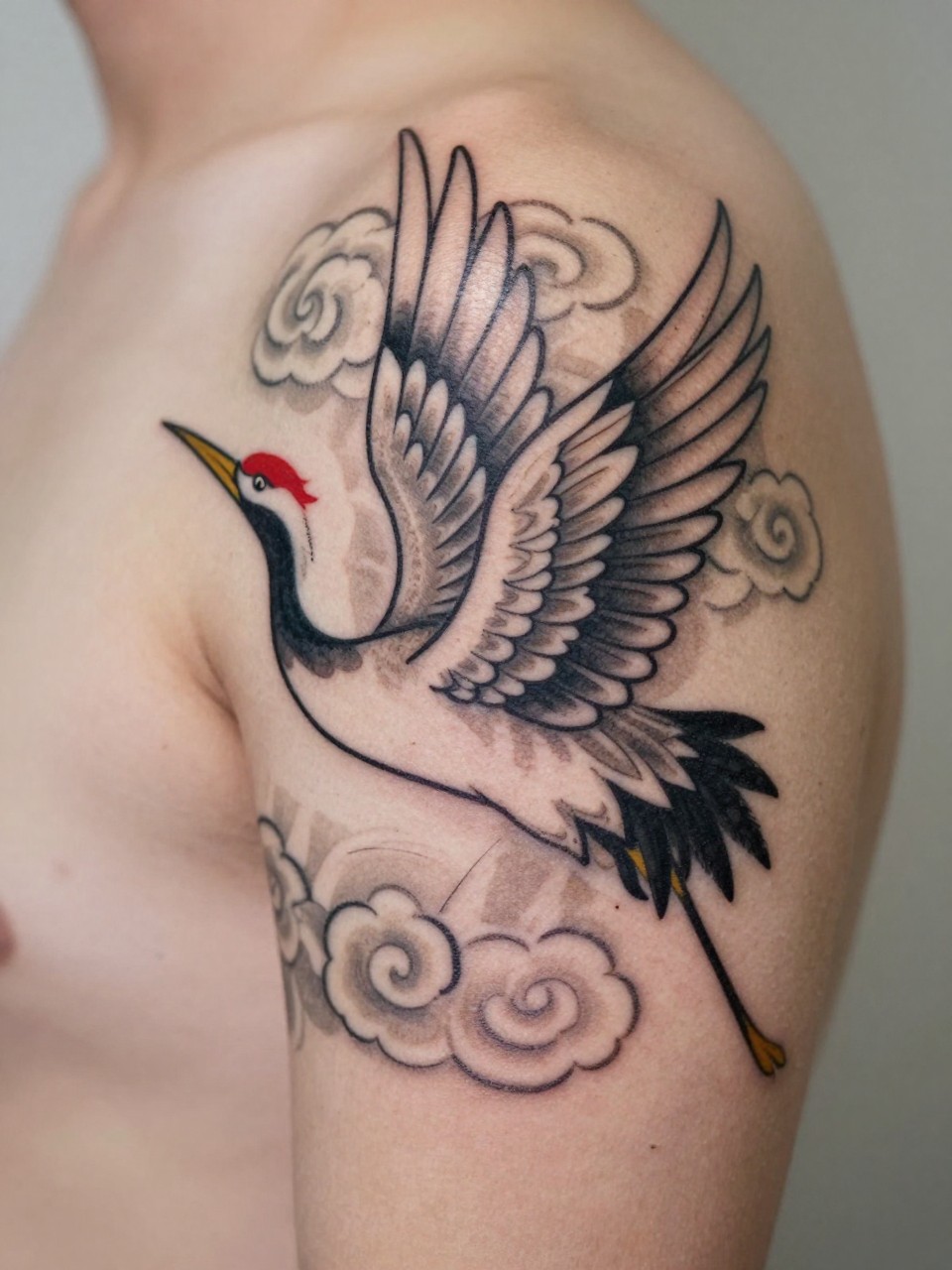 macro shot of a traditional Japanese crane and cloud tattoo on the forearm or shoulder, elegant bird shape, spread wings, cloud details, black and grey ink, clean traditional linework, realistic skin texture, design-first composition, soft neutral background, tattoo inspiration image (no watermarks on images)