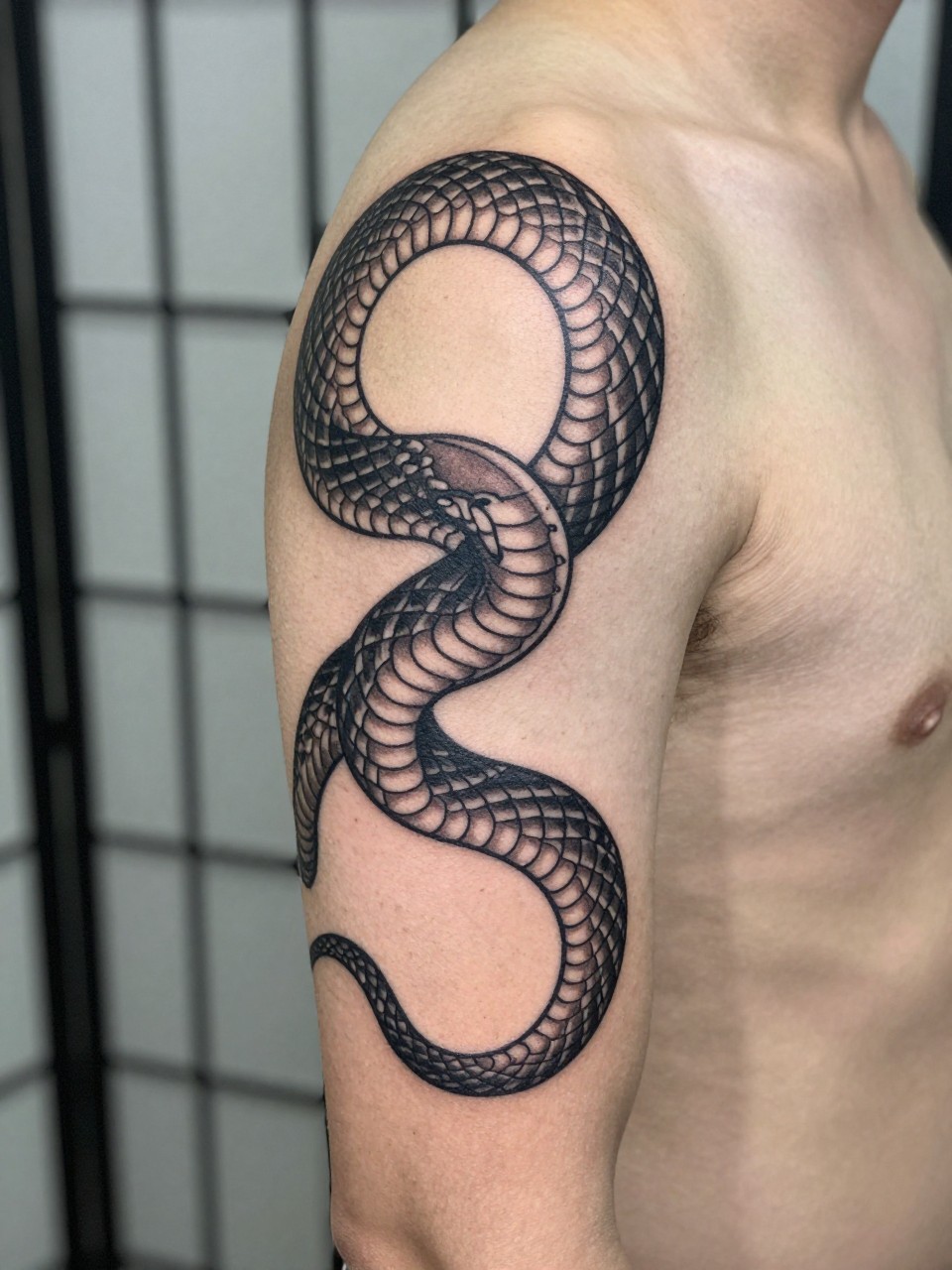 design-focused close-up of a Japanese snake armband tattoo on a man's upper arm, serpent body wrapped around the arm, fine scale detail, black and grey ink, bold linework, soft shading, realistic skin texture, minimal blurred background, modern tattoo inspiration photo (no watermarks on images)