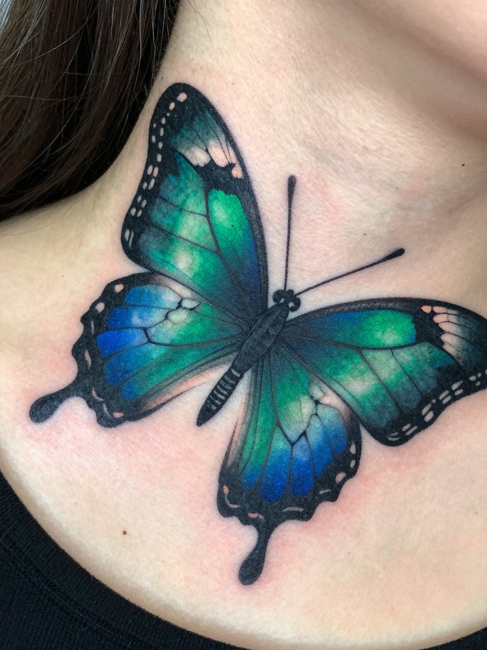 "Macro of the side neck: a butterfly tattoo with 'cracked' wing sections filled with deep emerald and sapphire color. Thick black leading lines create a sharp, jeweled effect."
