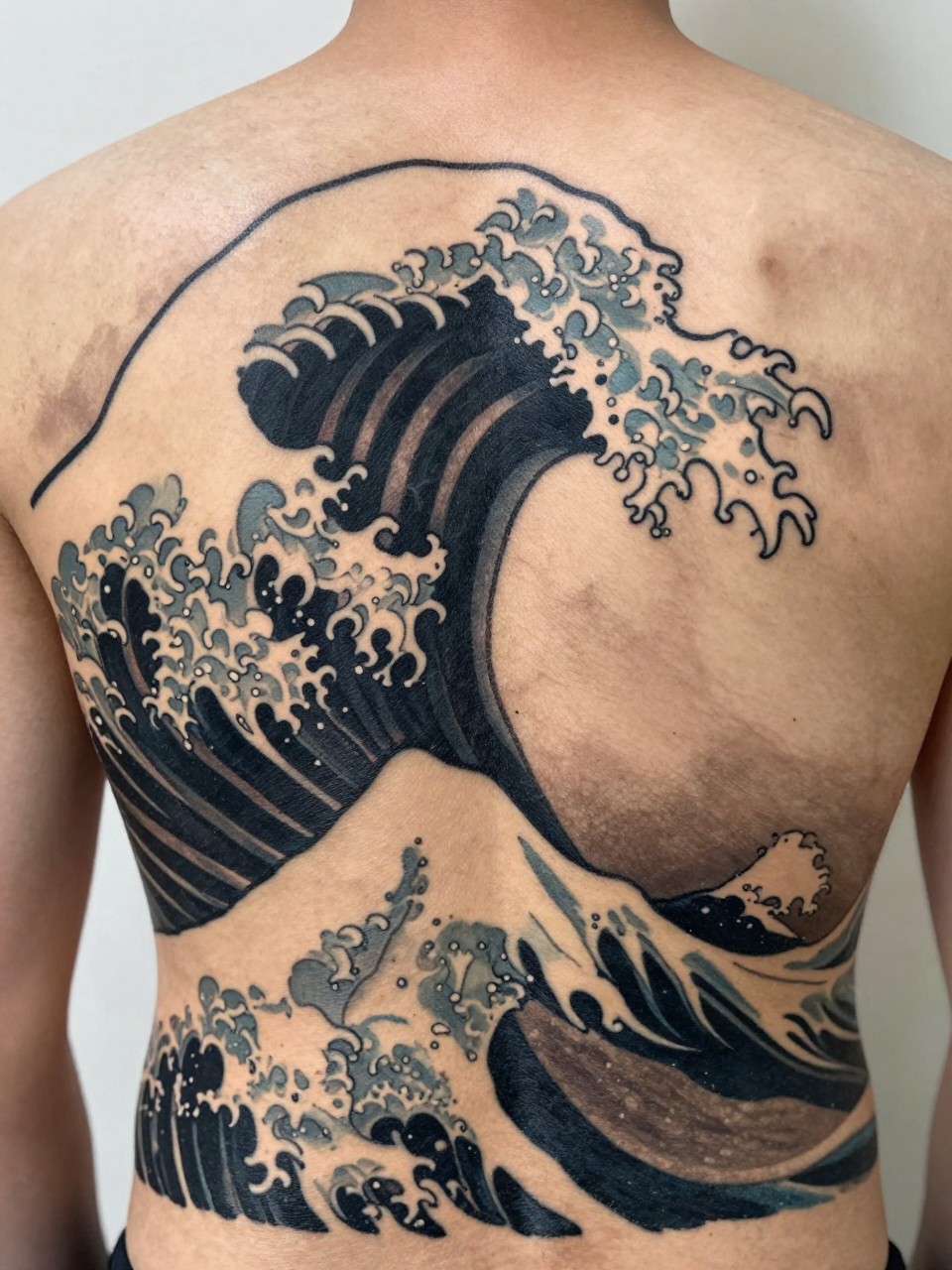 close-up of a clean full back Japanese wave tattoo panel, large layered cresting waves, black and grey ink, bold traditional linework, smooth shading, strong balanced composition, realistic skin texture, design-focused close-up, soft neutral background, modern tattoo photography (no watermarks on images)