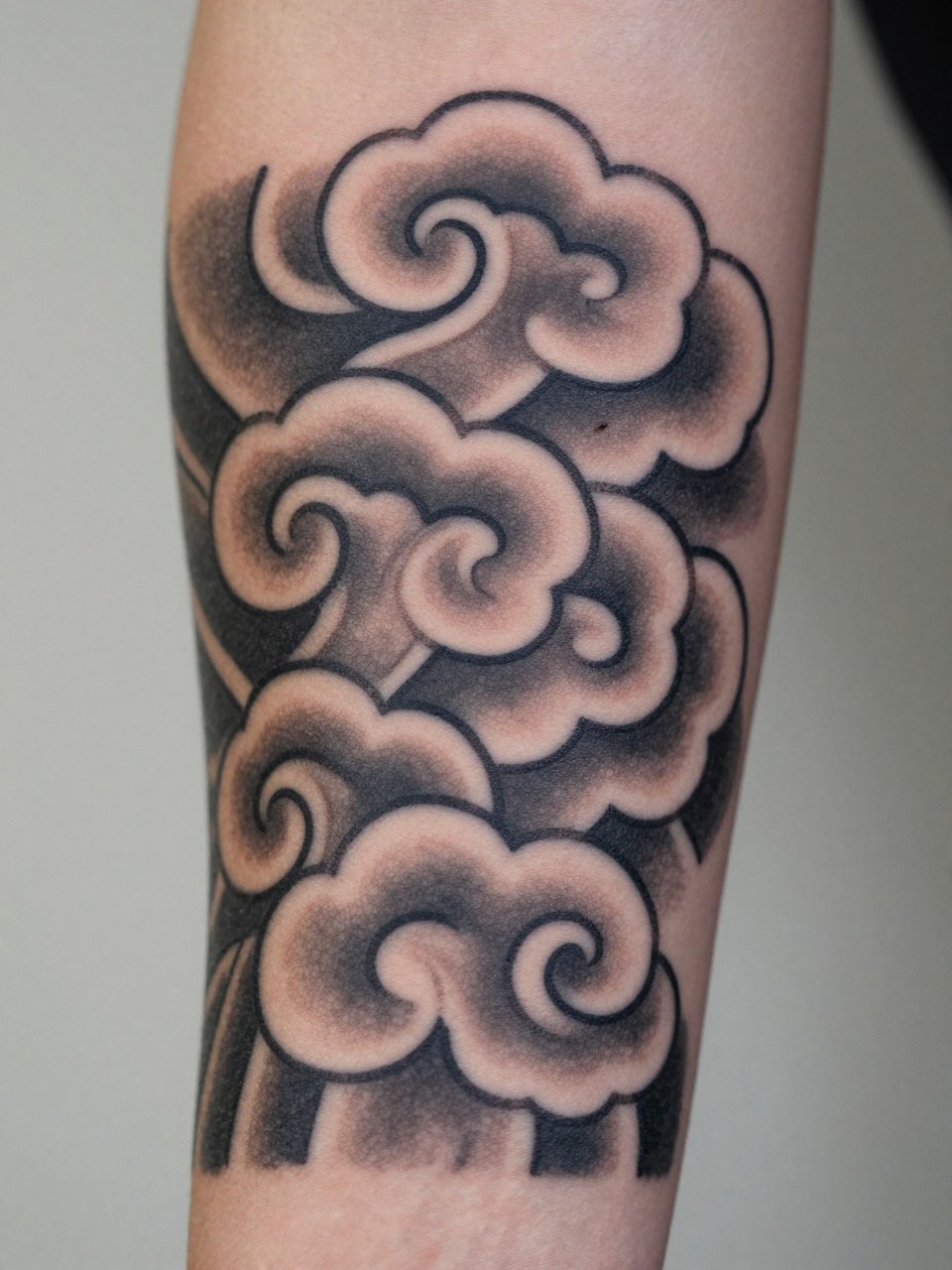 extreme close-up of a traditional Japanese wind bar cloud tattoo on the forearm, bold curved cloud forms, black and grey ink, crisp traditional linework, soft shading, clean balanced composition, realistic skin texture, design-focused close-up, soft neutral background, modern tattoo inspiration photography (no watermarks on images)