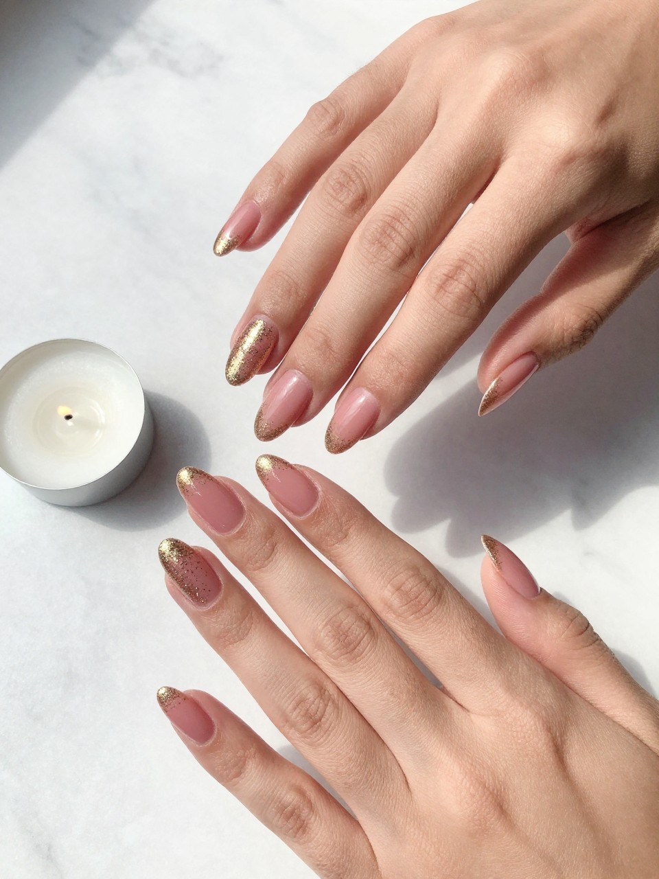 90-degree overhead top-down view of two feminine hands with almond medium nails.
The manicure features a rosy pink base with a gold glitter fade rising from the tips.
Include sparkling reflective detail with a glossy gel finish.

Hands are posed fingers gently spread.

Scene set on a white marble surface with a small birthday candle nearby.

Bright natural daylight with soft shadows, hyper-realistic lifestyle photography, sharp focus on nails, natural skin texture, realistic hands, no extra fingers.