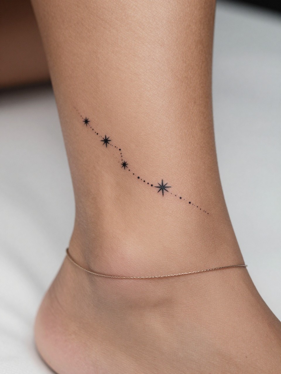 "extreme close-up of a small star trail tattoo on dark skin around the ankle, crisp black ink, tiny stars in a flowing pattern, fine line minimalist style, realistic skin texture, delicate anklet, soft blurred background, design-focused feminine tattoo inspiration photography (no watermarks on images)"