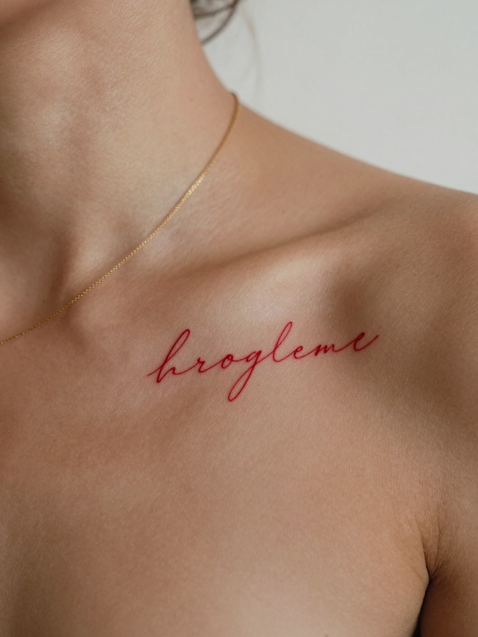  "extreme close-up of a small red script word tattoo on deep brown skin at the collarbone, clean red ink, neat fine line cursive lettering, elegant minimalist style, realistic skin texture, soft gold necklace, minimal blurred background, modern feminine tattoo inspiration photography (no watermarks on images)"