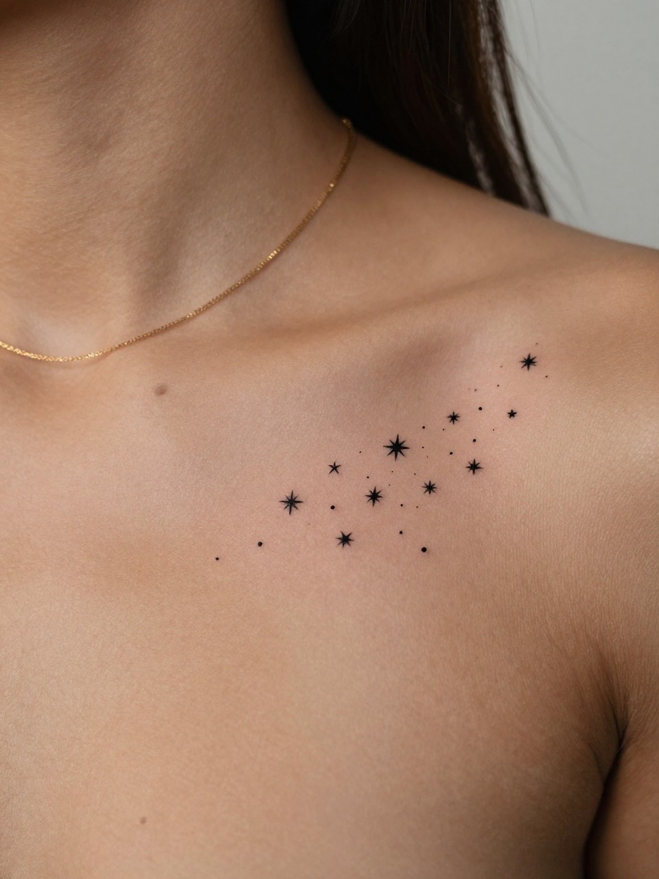 "design-focused close-up of a small star cluster tattoo on dark skin near the collarbone, tiny black ink stars, clean fine line work, minimal spacing, realistic skin texture, soft gold chain necklace, tight crop, minimal blurred background, feminine lifestyle tattoo inspiration photo (no watermarks on images)"