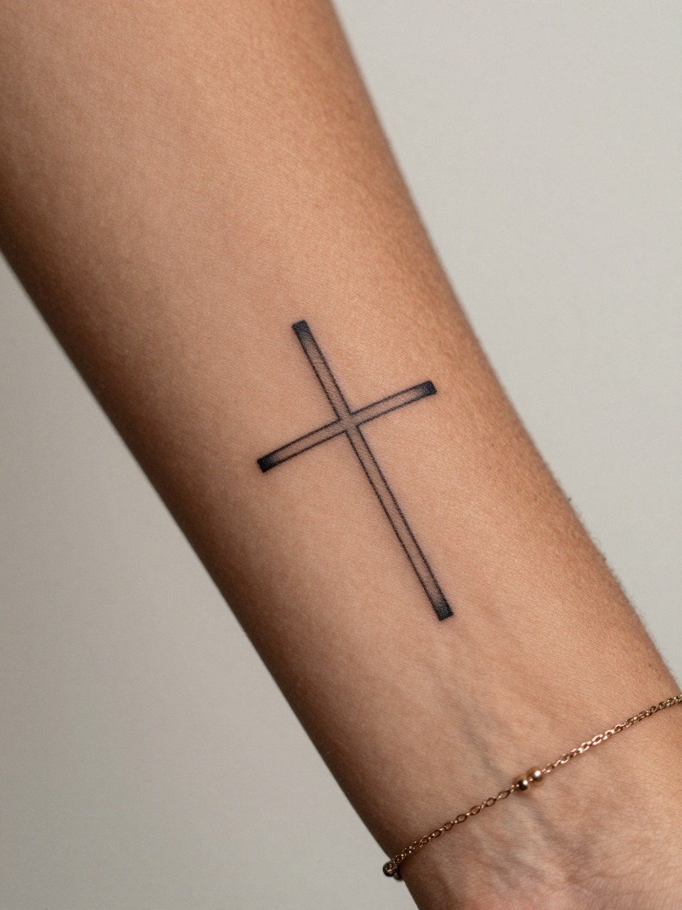 "macro shot of a minimal cross tattoo on rich brown skin at the inner wrist, crisp black ink, very small and clean linework, realistic skin texture, delicate bracelet, soft natural lighting, design-first tattoo image, minimal neutral background, feminine lifestyle tattoo photography (no watermarks on images)"