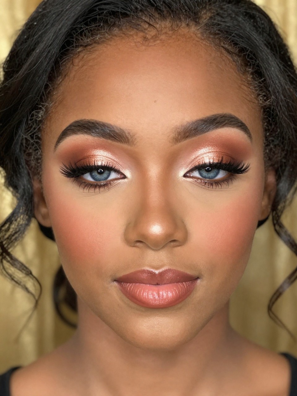 Super realistic close-up beauty portrait of a black teenage woman with blue eyes wearing lovely prom makeup, featuring soft copper shimmer eyeshadow across the lids, cinnamon crease blending, warm espresso lash-line definition, full curled lashes, warm rosy-peach blush, rosy nude satin lips, softly glowing skin texture, refined brows, shot from a front-facing beauty portrait, with warm diffused lighting that clearly reveals the copper shimmer, blue eyes, and satin lip finish, elegant curled hairstyle, blurred golden formal background, feminine modern beauty photography, latest iPhone photo quality.