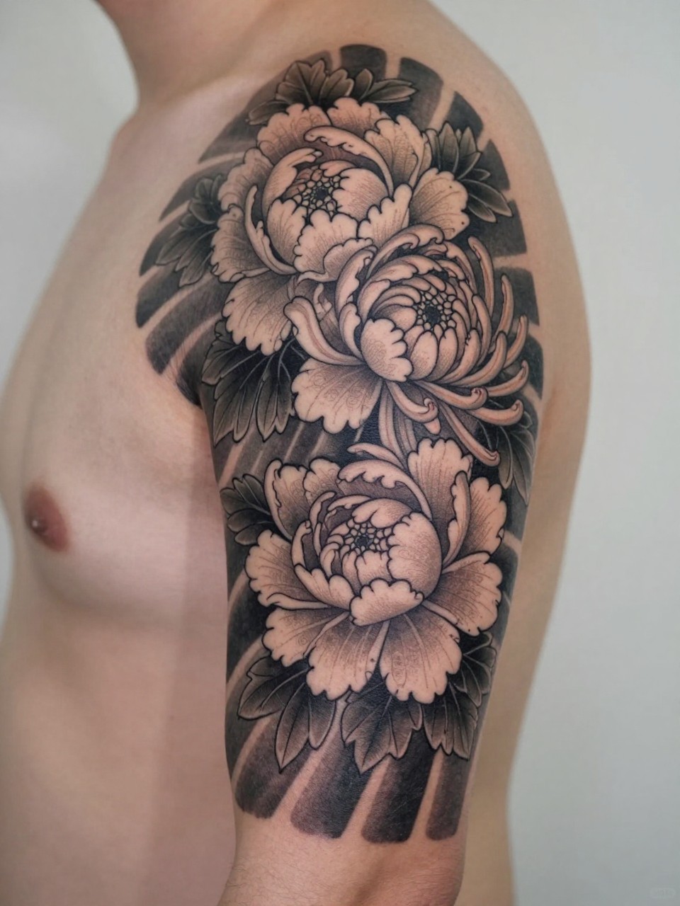 extreme close-up of a Japanese floral half sleeve starter tattoo on the upper arm, large peony and chrysanthemum blooms with leaf filler, black and grey ink, strong traditional linework, soft shading, realistic skin texture, soft minimal background, design-focused tattoo inspiration photography (no watermarks on images)