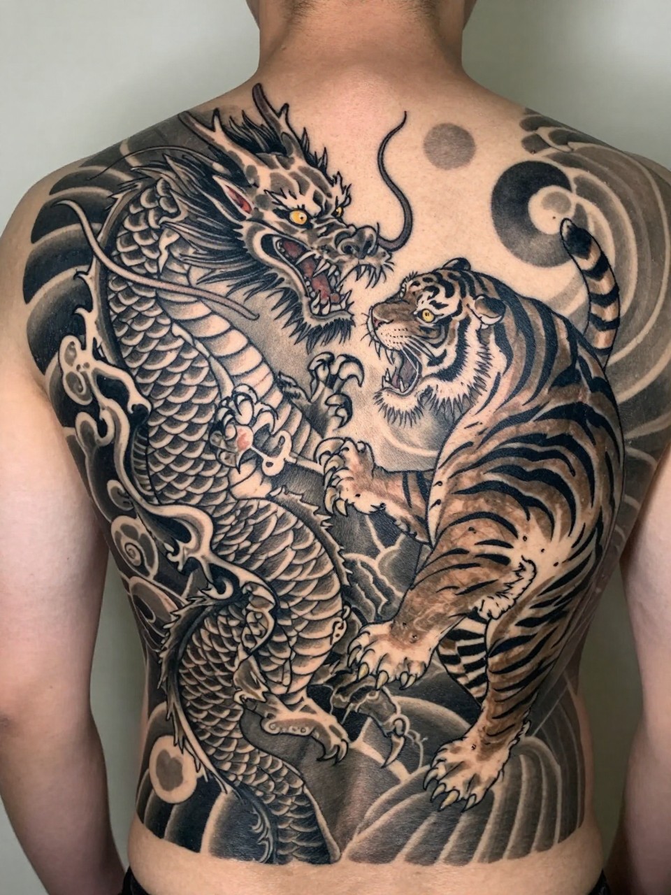 "macro shot of a full back Japanese dragon and tiger tattoo on a man, dragon and tiger in dynamic battle composition, black and grey ink, detailed scales and stripes, bold traditional linework, smooth shading, realistic skin texture, dramatic full back composition, soft neutral background (no watermarks on images)"