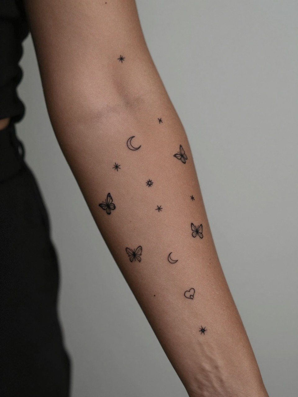 design-focused close-up of a full sleeve made of small tattoo symbols on deep brown skin, tiny stars hearts moons butterflies script words and flowers covering the arm, clean black ink, fine line minimalist style, realistic skin texture, sleeveless top visible, soft blurred background, modern feminine tattoo inspiration photography (no watermarks on images)