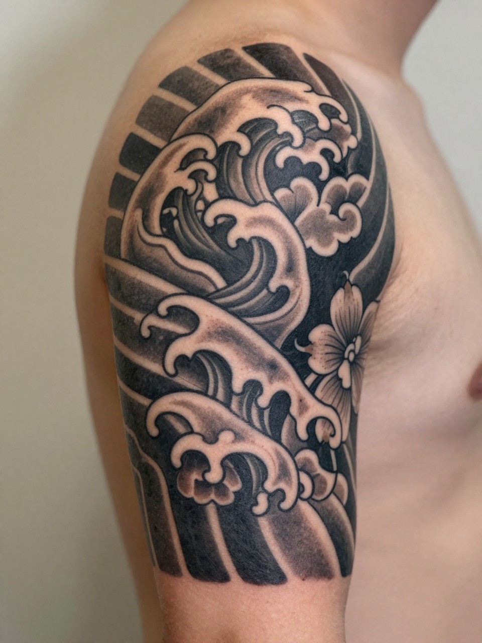 macro shot of a mixed Japanese motif armband tattoo on a man's upper arm, waves leaves clouds and floral details wrapping around the arm in one balanced band, black and grey ink, bold traditional-inspired linework, realistic skin texture, design-first tattoo image, soft neutral background, tattoo inspiration image (no watermarks on images)