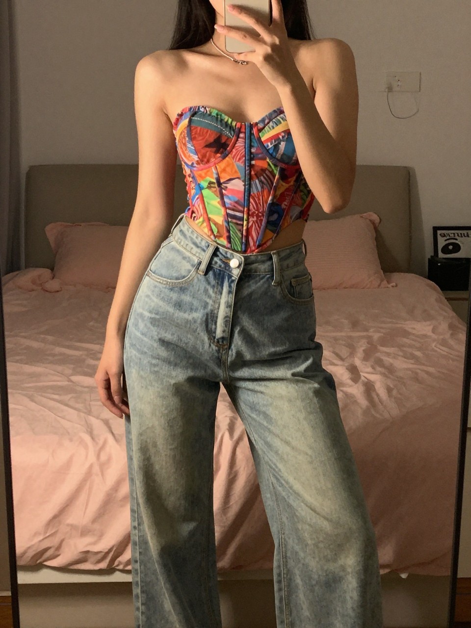 iPhone mirror selfie of a woman in a colorful corset top and wide-leg pants, posing with confidence, cropped at the neck so face doesn't show, in a feminine-themed bedroom, warm moody lighting, iPhone photo quality.