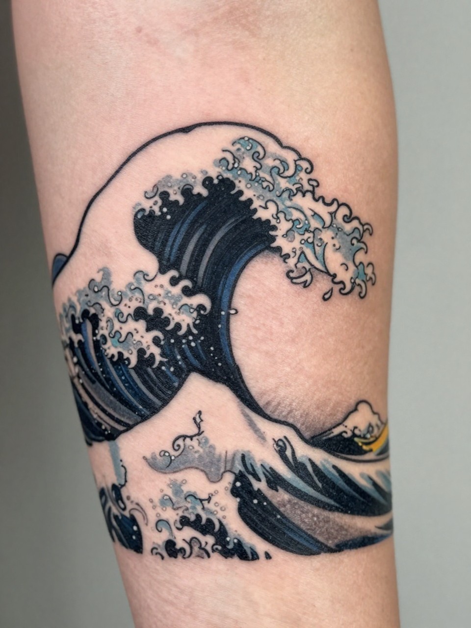 extreme close-up of a clean Japanese cresting wave tattoo on the forearm, bold curling wave shape, black and grey ink, crisp traditional linework, soft shading, minimalist composition, realistic skin texture, design-focused close-up, soft neutral background, modern tattoo inspiration photography (no watermarks on images)
