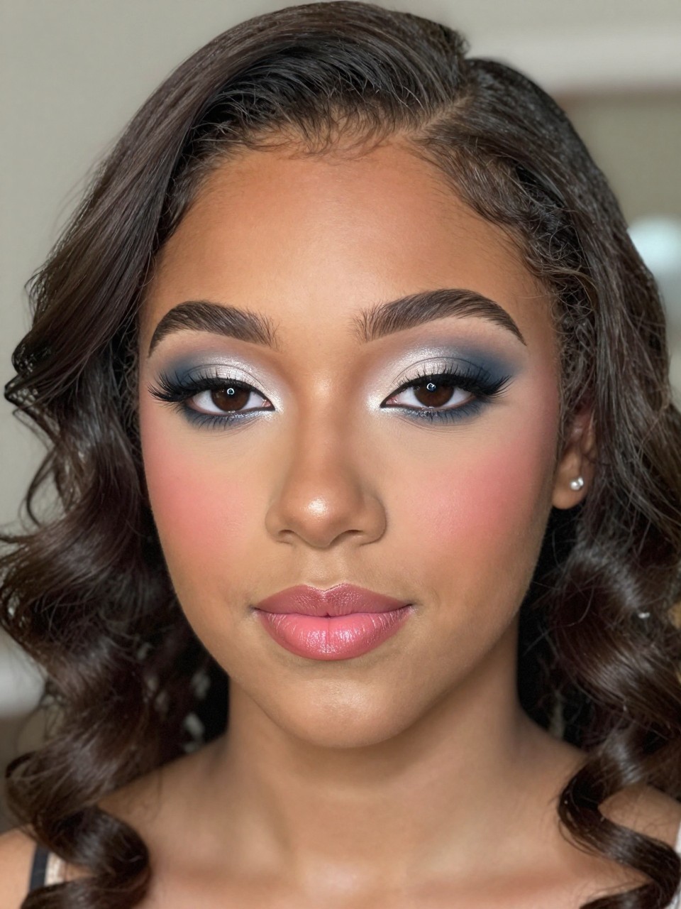 Super realistic close-up beauty portrait of a teenage black woman with brown eyes wearing cute prom makeup, featuring soft blue-gray eyeshadow across the lids, silver-taupe blending, a whisper of soft charcoal at the outer corners, defined volumized lashes, muted pink blush, pearl-champagne highlight, pink nude satin lips, polished brows, realistic skin texture with a smooth luminous finish, shot from a front-facing beauty portrait, with cool elegant lighting that clearly reveals the blue-gray eye tones and satin lips, softly styled prom curls, softly blurred formal evening background, feminine modern beauty photography, latest iPhone photo quality.