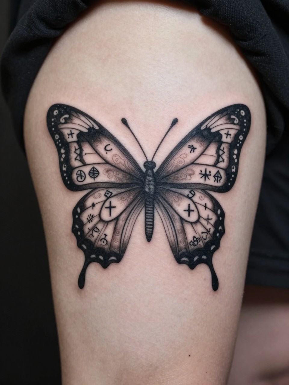 "Close-up of a thigh tattoo: a butterfly's wings filled with intricate, esoteric alchemy symbols in a symmetrical pattern. Clean black lines, cryptic and powerful."