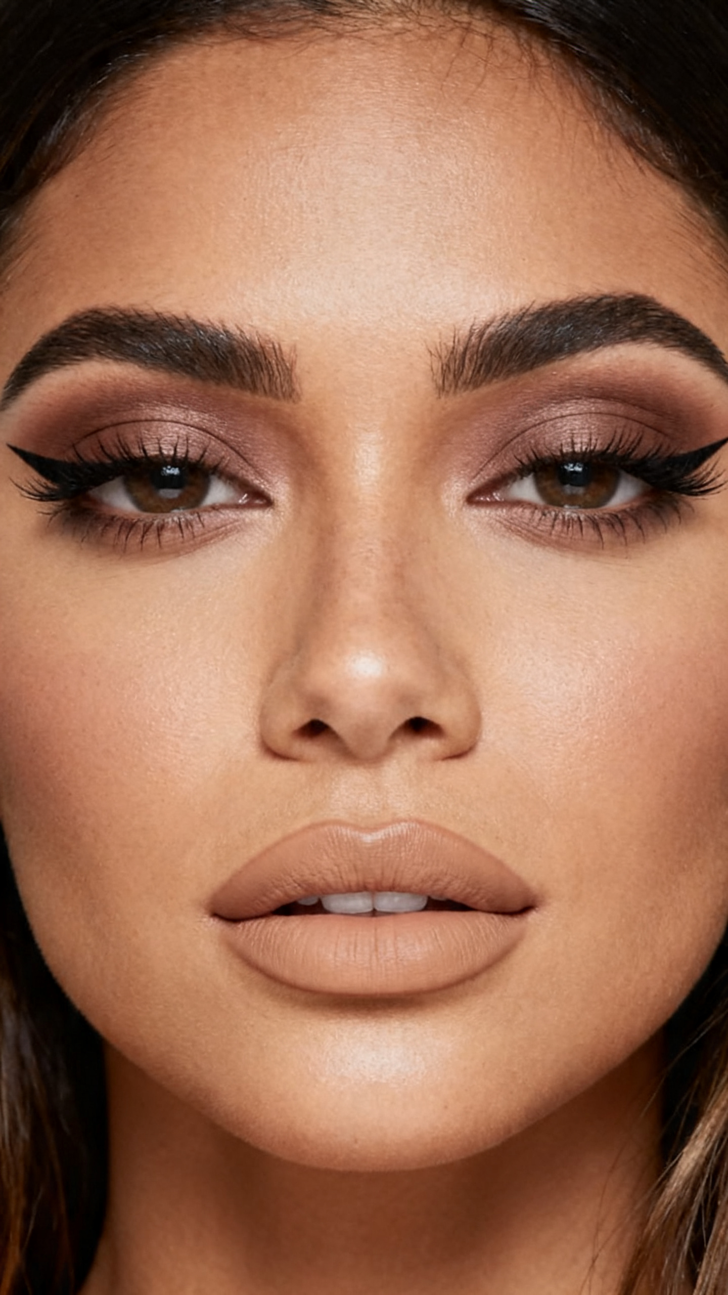 Super realistic close-up beauty portrait of a latina woman wearing espresso winged eyeliner with softly blended taupe-brown eyeshadow, satin skin, soft beige satin lips, clean volumized lashes, and shaped brows, shot from a front-facing portrait, with soft studio lighting that clearly reveals the makeup texture and color, realistic skin texture, softly styled hair, minimal background, feminine modern beauty photography, latest iPhone photo quality.