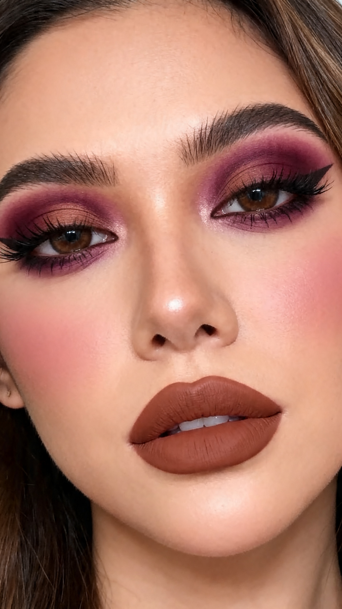 Super realistic close-up beauty portrait of a woman wearing burgundy pirate smoky eyes with plum and brown depth, smudged espresso liner, muted mauve-brown blush, soft brown nude lips, and long lashes, shot from a front-facing portrait, with soft vanity lighting that clearly reveals the makeup texture and color, realistic skin texture, softly styled hair, minimal background, feminine modern beauty photography, latest iPhone photo quality.