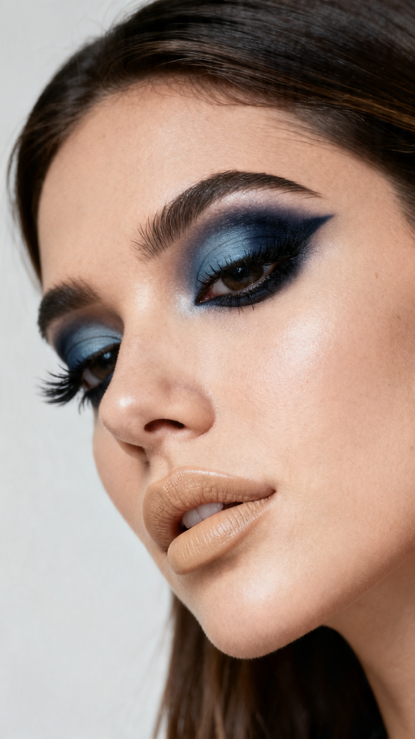 Super realistic close-up beauty portrait of a woman wearing smoked navy pirate eyes with slate-blue blending, blackened navy liner, smooth satin skin, soft beige satin lips, and defined lashes, shot from a three-quarter view, with diffused beauty studio lighting that clearly reveals the makeup texture and color, realistic skin texture, sleek hair framing the face, minimal background, feminine modern beauty photography, latest iPhone photo quality.