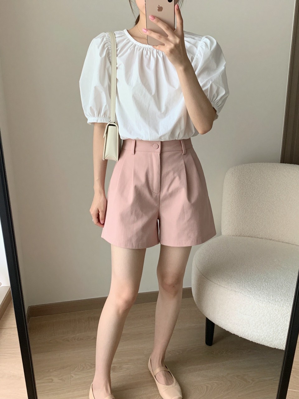 IMAGE_PROMPT: mirror selfie of a woman wearing a white puff-sleeve cotton top, blush pink tailored shorts, nude ballet flats, small cream shoulder bag, and glossy pink lip makeup, clearly showing the same clothing items listed in the Outfit Pieces section, holding a phone in front of a mirror, cropped at the NECK so the face does not show, relaxed casual selfie pose, in a modern living room mirror setup, soft morning light, with accent chair beside the mirror, latest iPhone photo quality.