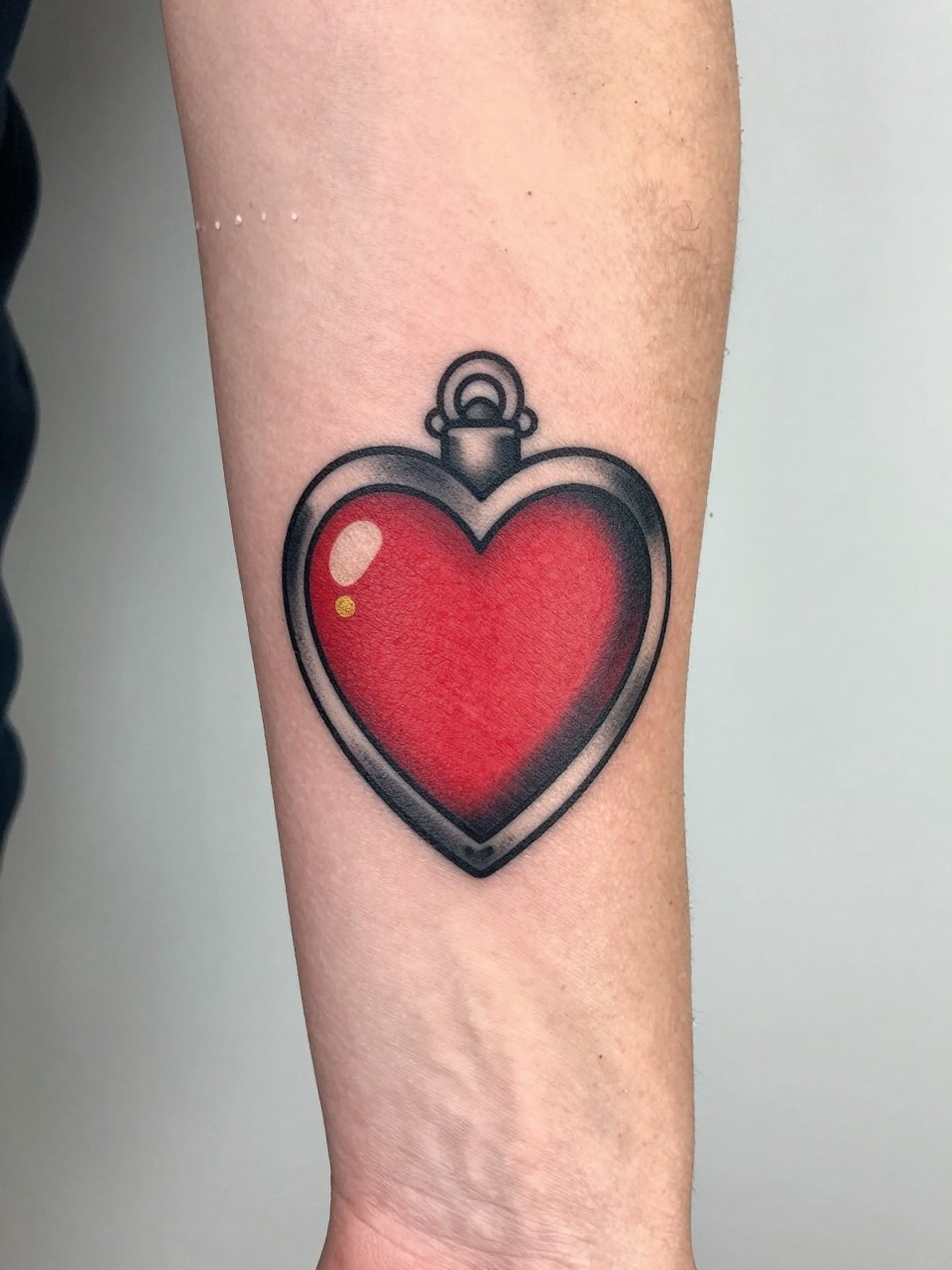 Image Prompt: "Extreme close-up of an American traditional heart locket tattoo on the forearm, bold black linework, red heart-shaped locket, tiny gold detail, small shine marks, soft black shading, feminine design, delicate rings visible near the hand, clean minimal background, realistic skin texture, tattoo design as hero"
