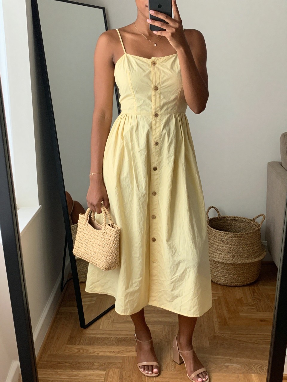 IMAGE_PROMPT: mirror selfie of a black woman wearing a butter yellow button-front cotton sundress, nude block-heel sandals, woven mini handbag, delicate gold bracelet, and glossy nude lip makeup, clearly showing the same clothing items listed in the Outfit Pieces section, holding a phone in front of a mirror, cropped at the NECK so the face does not show, relaxed casual selfie pose, in a cozy living room with a leaning floor mirror, natural window light, with woven basket near the mirror, latest iPhone photo quality.