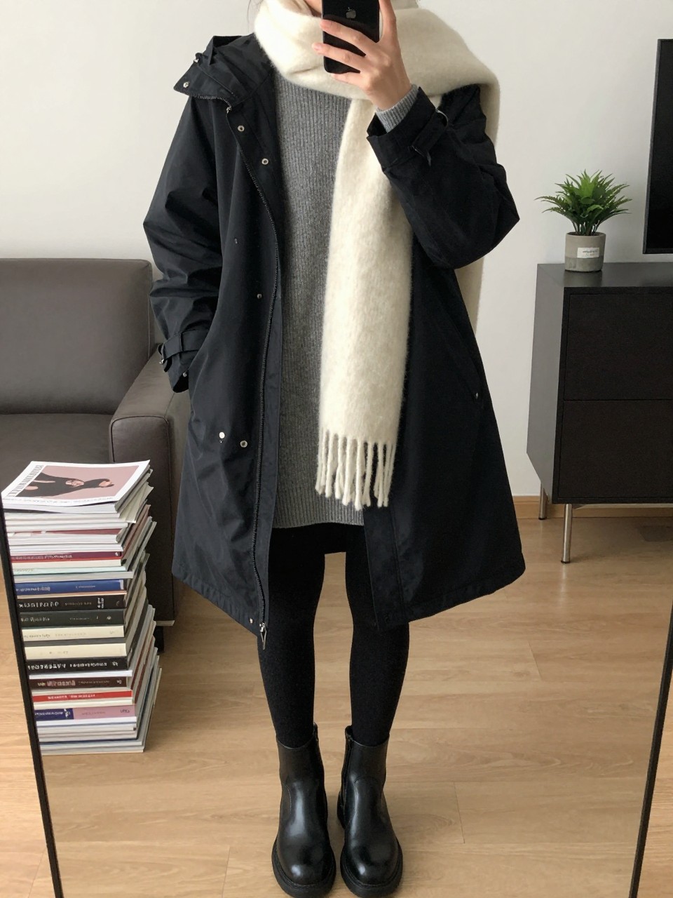 mirror selfie of a woman wearing a black waterproof parka over a gray ribbed sweater dress, black fleece-lined tights, black waterproof ankle boots, and a soft cream scarf, clearly showing the same clothing items, colors, fabrics, and accessories listed in the Outfit Pieces section, holding a phone in front of a mirror, cropped at NECK so the face does not show, with a relaxed casual selfie pose, in a stylish city apartment, soft indoor lighting, including a stack of fashion magazines on a side table and a small plant on a dresser, latest iPhone photo quality.
