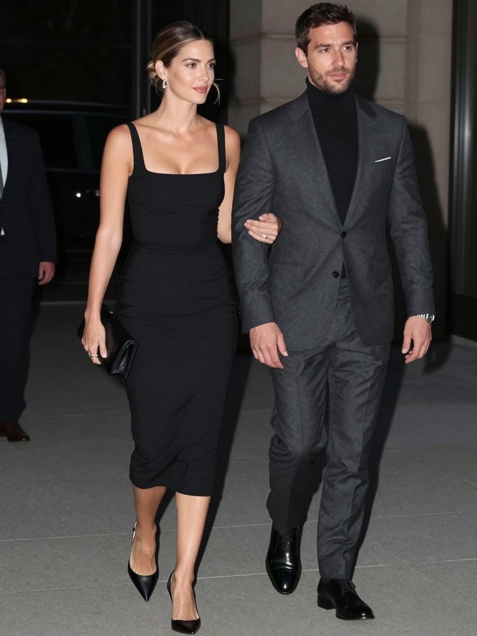 Outfit Image Prompt:
A modern couple walking into a semi formal evening event, realistic phone-camera fashion photo with soft flash and gentle evening shadows, natural skin texture, soft focus background, relaxed candid movement. The woman wears a fitted black midi dress with a square neckline, subtle ruching, black pointed-toe slingback heels, a small black clutch, silver drop earrings, and a sleek low bun with a few loose strands. The man wears a charcoal suit with a black fine-knit turtleneck, polished black dress shoes, a silver watch, and a clean pocket square. Their outfits coordinate through dark tones and sharp lines without looking like a costume. Show normal fabric folds, real-life fit, slight movement in the clothing, no over-sharpening, no glossy plastic skin, no waxy faces, no overly perfect hands, no airbrushed finish, no watermarks on images.