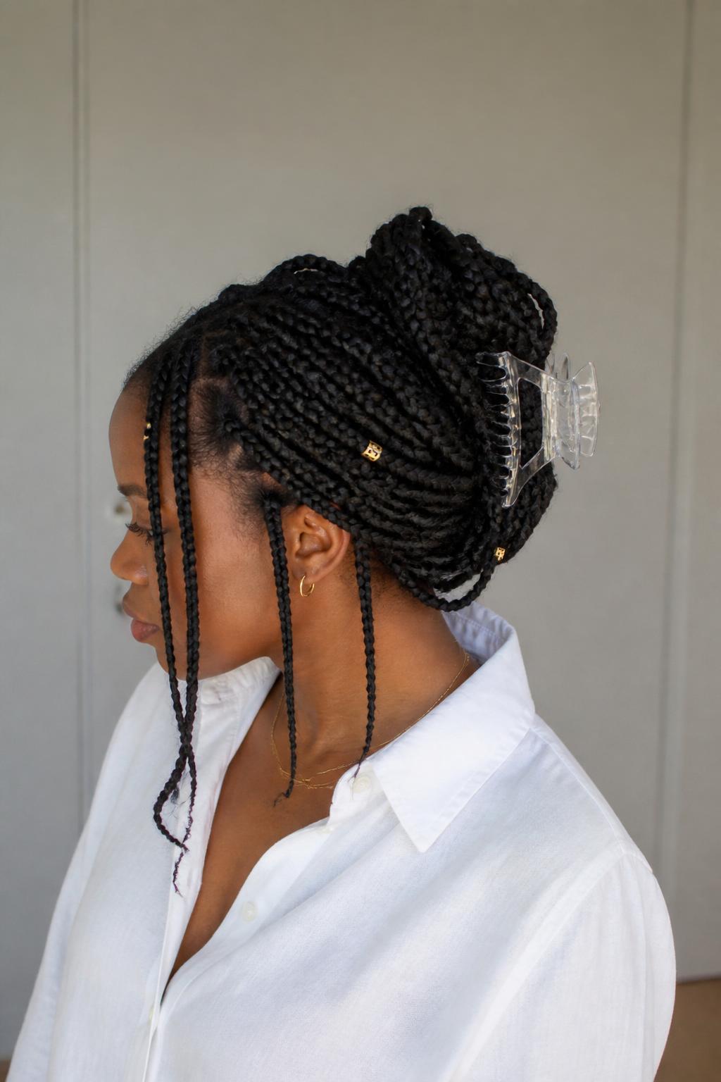 Image Prompt:
A realistic hairstyle photo of a black woman with long box braids styled into a claw clip twist, braids gathered and twisted upward with a large clear acrylic claw clip holding the middle, a few front braids left loose, gold cuffs on select braids, casual white button-down shirt, soft daylight, clean neutral background, modern protective hairstyle inspiration, high-resolution photo, no text, no watermark.