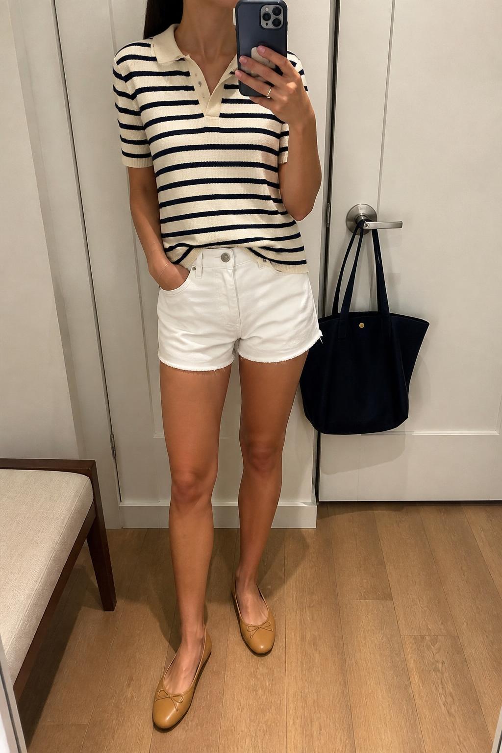 IMAGE_PROMPT: mirror selfie of a woman wearing a cream and navy striped knit polo, white denim shorts, tan leather ballet flats, navy canvas tote bag, and sleek low ponytail, clearly showing the same clothing items listed in the Outfit Pieces section, holding a phone in front of a mirror, cropped at the NECK so the face does not show, relaxed casual selfie pose, in a minimal dressing room, soft indoor lighting, with handbag hanging on a door handle, latest iPhone photo quality.