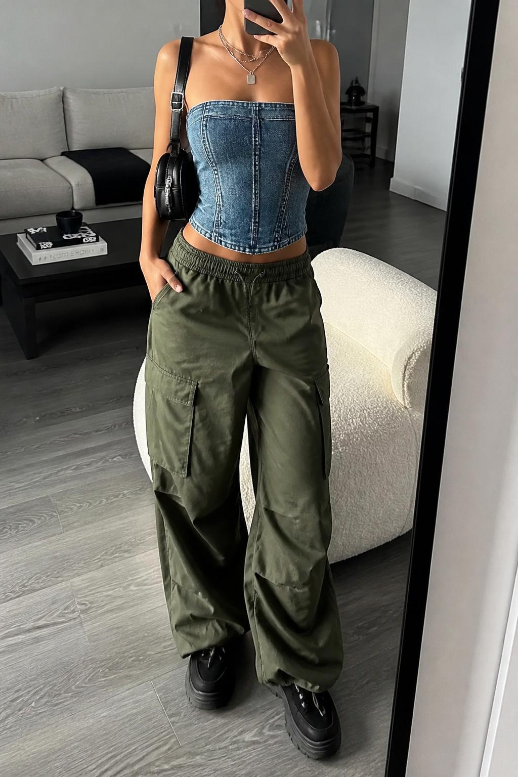 IMAGE_PROMPT: mirror selfie of a woman wearing a blue denim corset top, olive cargo parachute pants, black platform sneakers, mini black backpack, and silver layered necklaces, clearly showing the same clothing items listed in the Outfit Pieces section, holding a phone in front of a mirror, cropped at the NECK so the face does not show, relaxed casual selfie pose, in a modern living room mirror setup, soft indoor lighting, with accent chair beside the mirror, latest iPhone photo quality.
