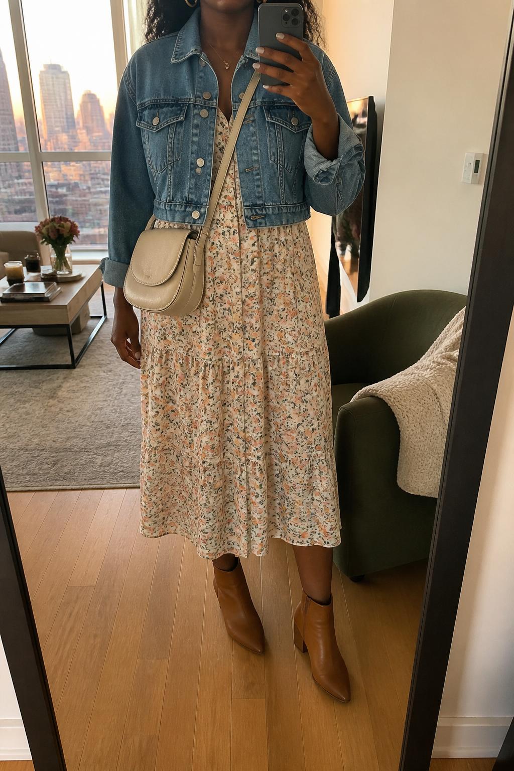 IMAGE_PROMPT: mirror selfie of a black woman wearing a blue cropped denim jacket, soft floral cotton midi dress, tan leather ankle boots, cream crossbody bag, and small gold hoops, clearly showing the same clothing items listed in the Outfit Pieces section, holding a phone in front of a mirror, cropped at the NECK so the face does not show, relaxed casual selfie pose, in a stylish city apartment living room, evening golden hour, with accent chair beside the mirror, latest iPhone photo quality.