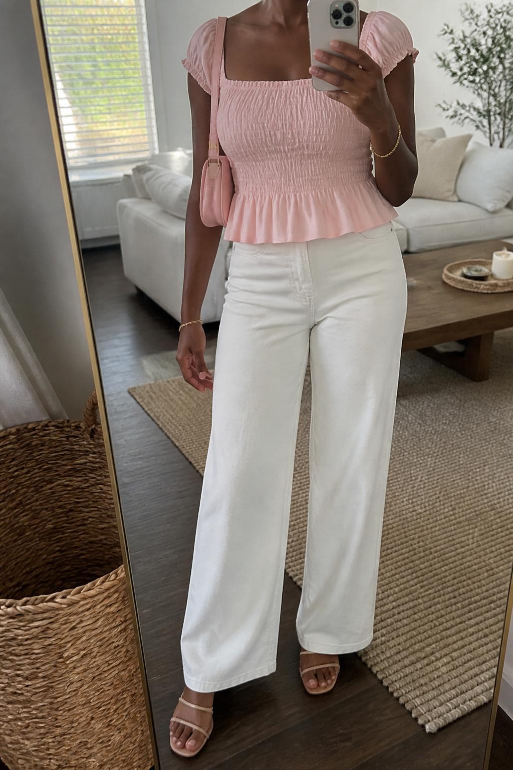 IMAGE_PROMPT: mirror selfie of a black woman wearing a soft pink smocked square-neck top, white wide-leg jeans, nude strappy flat sandals, pink mini shoulder bag, and delicate gold bracelet, clearly showing the same clothing items listed in the Outfit Pieces section, holding a phone in front of a mirror, cropped at the NECK so the face does not show, relaxed casual selfie pose, in a cozy living room with a leaning floor mirror, natural window light, with woven basket near the mirror, latest iPhone photo quality.