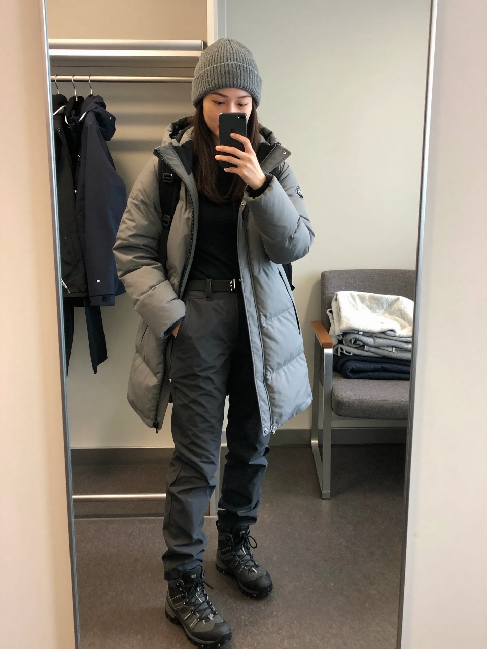 Outfit Image Prompt:
mirror selfie of a woman wearing a gray lightweight puffer coat, black thermal long-sleeve top, charcoal waterproof hiking pants, black waterproof hiking boots, a gray knit beanie, and a black backpack, holding a phone in front of a mirror, cropped at NECK so the face does not show, relaxed casual selfie pose, in a cruise cabin mirror setup with soft indoor lighting, including a clothing rack with garments behind and a folded blanket on a chair, realistic latest iPhone photo quality, natural and practical travel styling.