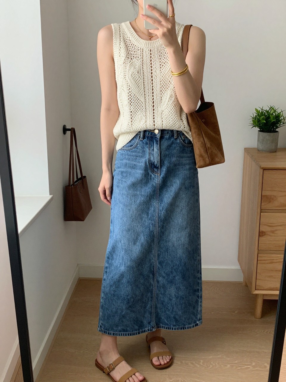 Outfit Image Prompt:
mirror selfie of a woman wearing a cream crochet sleeveless tank top with a lined front, medium-wash denim maxi skirt with a front slit, tan flat sandals, small brown suede shoulder bag, and gold bangle bracelets, holding a phone in front of a mirror, cropped at NECK so the face does not show, relaxed summer selfie pose, in a minimal dressing room, natural window light, with a handbag hanging on a door handle and a small plant on a dresser, realistic latest iPhone photo quality, casual NYC outfit.