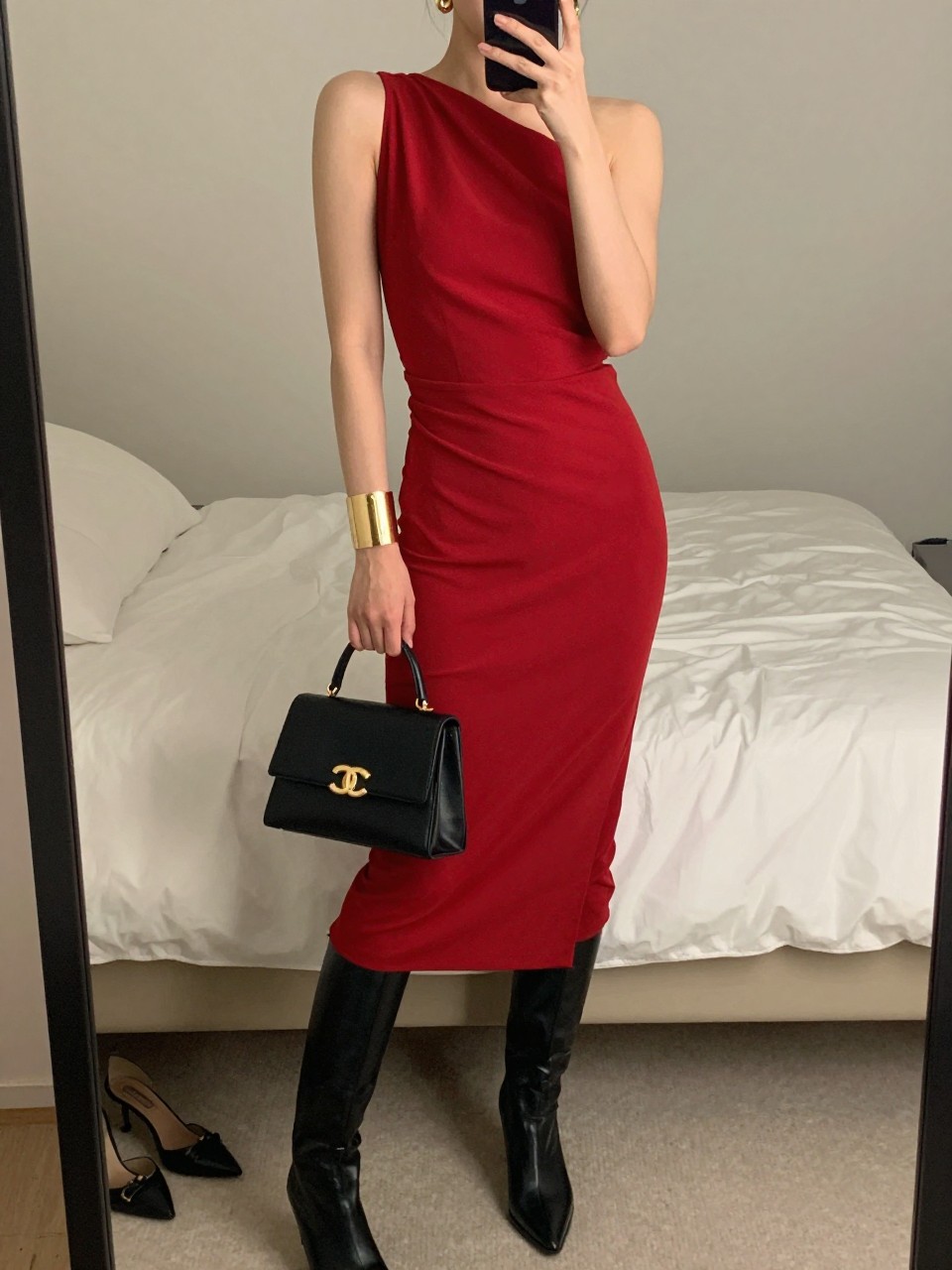 Outfit Image Prompt:
mirror selfie of a woman wearing a red draped asymmetrical midi dress, black leather knee-high boots, black structured mini bag, gold cuff bracelet, and small gold hoop earrings, holding a phone in front of a mirror, cropped at NECK so the face does not show, relaxed editorial selfie pose, in a feminine-themed bedroom, soft indoor lighting, with soft pillows on an unmade bed and a pair of heels on the floor nearby, realistic latest iPhone photo quality, high fashion NYC date night look.