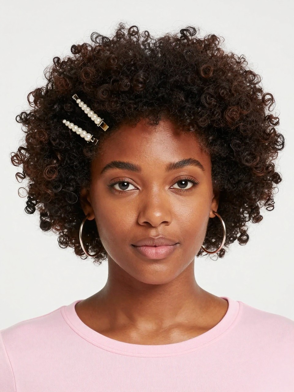 Image Prompt:
A realistic portrait photo of a black woman with medium-length coily natural hair styled into a high curly puff, two small pearl barrette clips placed along one side near the hairline, full textured puff shape, soft laid edges, warm brown skin, hoop earrings, pastel pink top, bright clean studio background, playful natural hair inspiration, high-resolution DSLR photo, no text, (no watermarks on images)