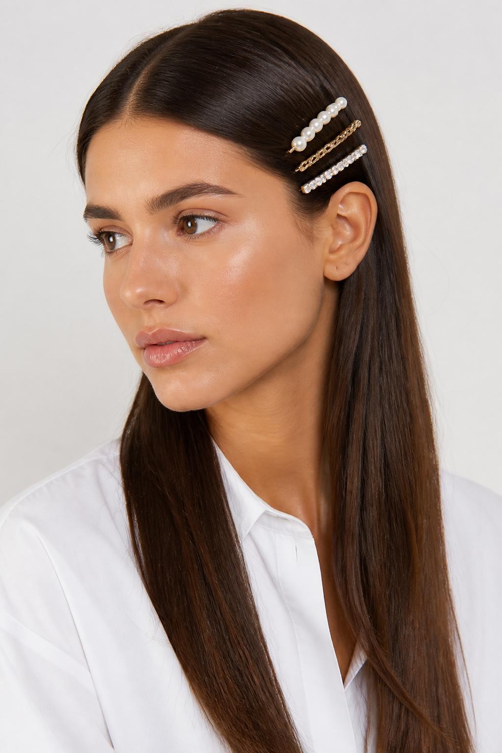 Image Prompt:
A realistic editorial beauty photo of a woman with long sleek dark brown straight hair styled with three slim barrettes stacked neatly on one side above the ear, mixed pearl, gold, and crystal finishes, clean center part, glossy straight lengths, white tailored shirt, minimal studio background, soft neutral lighting, modern accessory-focused hairstyle inspiration, high-resolution DSLR photo, no text, (no watermarks on images)
