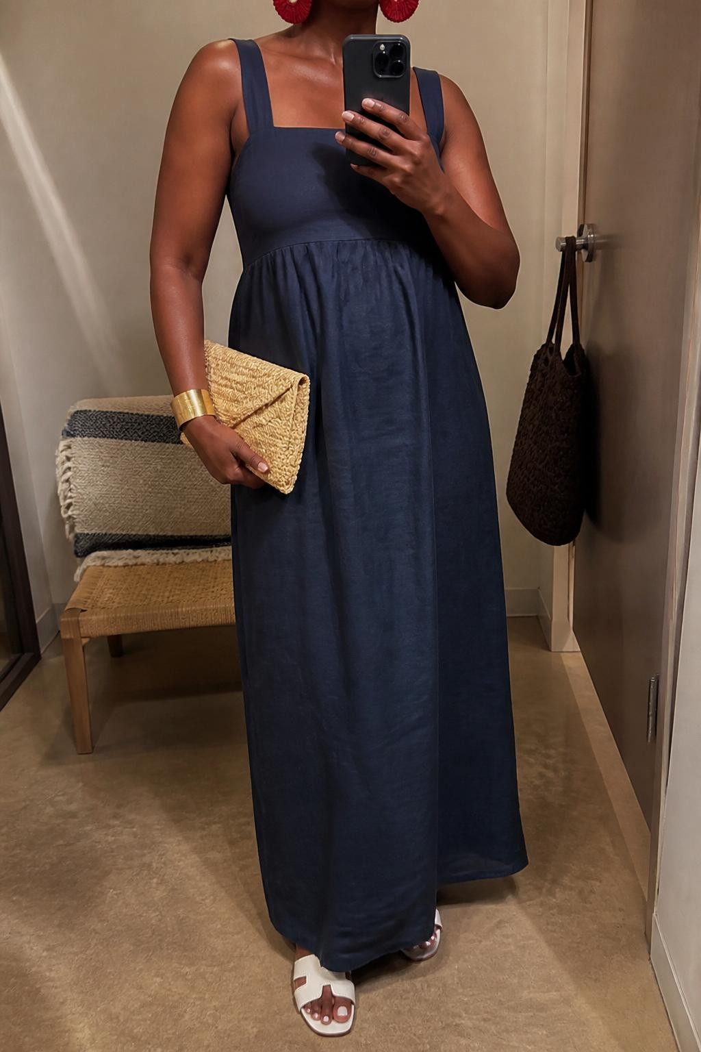 Outfit Image Prompt:
mirror selfie of a Black woman with rich deep brown skin wearing a navy linen maxi dress, red raffia statement earrings, white flat sandals, a natural straw clutch, and a gold cuff bracelet, clearly showing the exact clothing items and accessories listed, holding a phone in front of a mirror, cropped at NECK so the face does not show, relaxed casual selfie pose, in a minimal dressing room, evening golden hour lighting, with a handbag hanging on a door handle and a folded blanket on a chair, realistic latest iPhone photo quality, natural skin texture.
