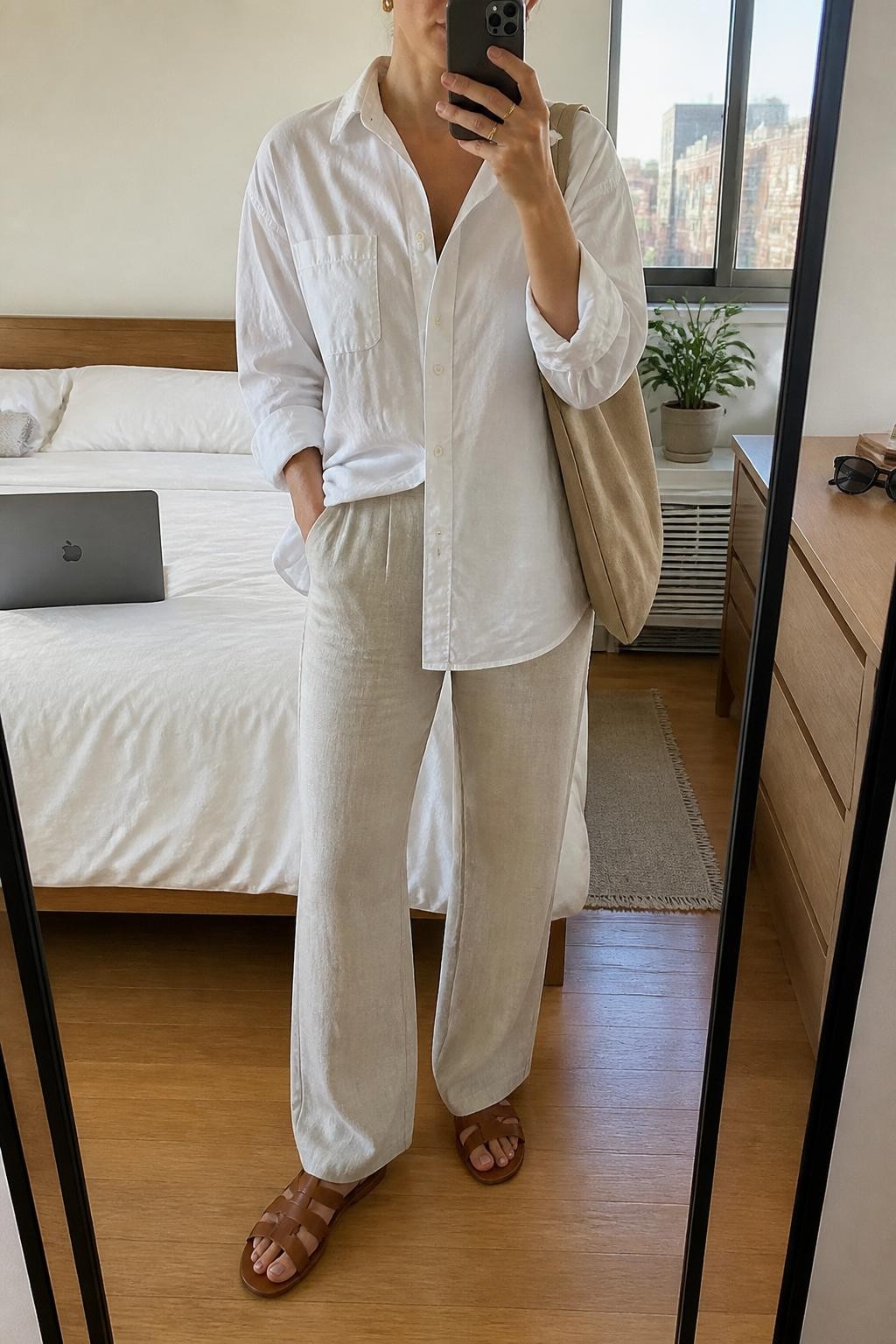 Outfit Image Prompt:
mirror selfie of a woman wearing a white oversized poplin button-down shirt, beige linen straight-leg trousers, brown leather fisherman sandals, a tan canvas tote bag, and small gold stud earrings, holding a phone in front of a mirror, cropped at NECK so the face does not show, relaxed casual selfie pose, in a stylish city apartment, natural window light, with a laptop on the bed and sunglasses placed on a dresser, realistic latest iPhone photo quality, soft natural vacation styling.
